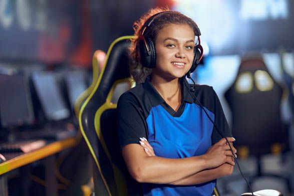 Portrait of a happy teenage mixed race girl, female cyber sport gamer wearing headphones looking at camera and smiling while participating in eSports tournament, playing online video games