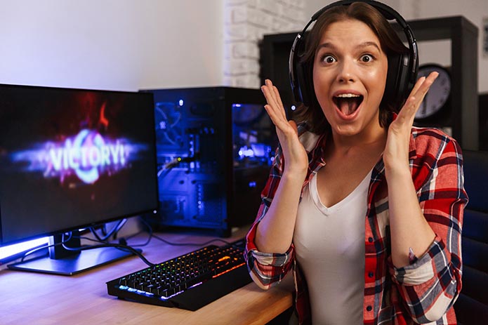 Excited girl gamer sitting at the table, playing online games